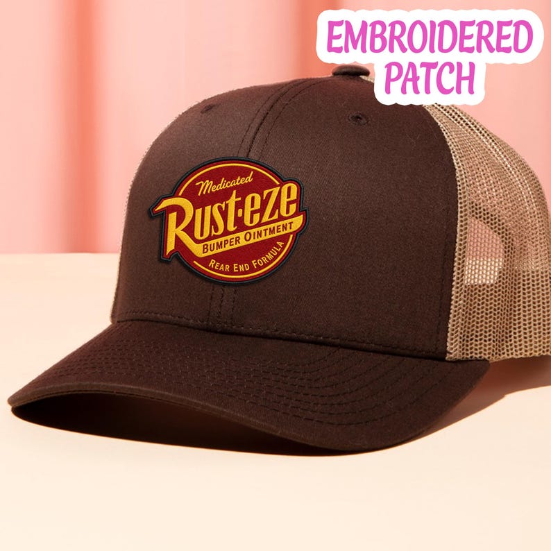 May include: A brown trucker hat featuring a circular embroidered patch on the front. The patch displays the text Medicated Rust-eze Bumper Ointment Rear End Formula in yellow and red. The hat has a solid brown front panel and a tan mesh back.