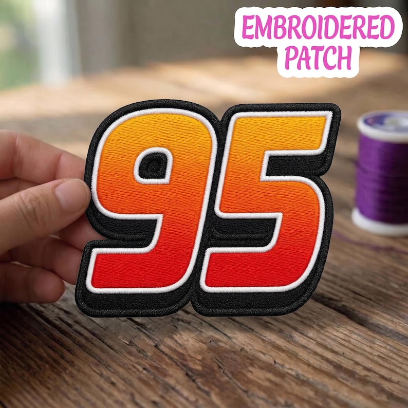 May include: An embroidered patch featuring the number 95 in a bold, block font. The numbers display a gradient color transition from yellow at the top to orange in the middle and red at the bottom, outlined in white and a thick black border.