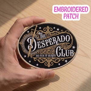 May include: Oval embroidered patch with the text "The Desperado Club" in white and gold, featuring a sword and decorative flourishes on a black background. The patch also includes the phrase "So Fun It Hurts" and small star accents.
