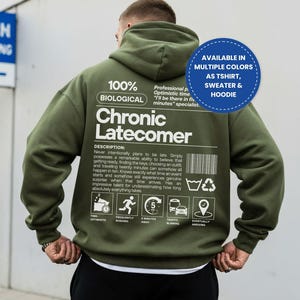 May include: An olive green hooded sweatshirt featuring white text on the back that reads 100% BIOLOGICAL Chronic Latecomer, along with a detailed description, a barcode, laundry symbols, and five icons representing time, rushing, 5 minutes, traffic, and arriving.