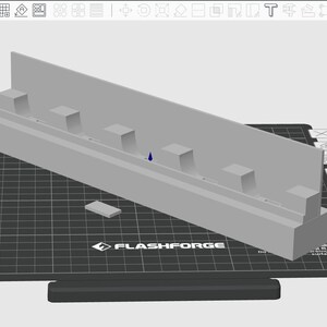 May include: A light gray 3D-printed object, possibly a component or model, featuring a rectangular base with a raised section and several small, square protrusions. It sits on a black grid-patterned surface with the "FLASHFORGE" logo.