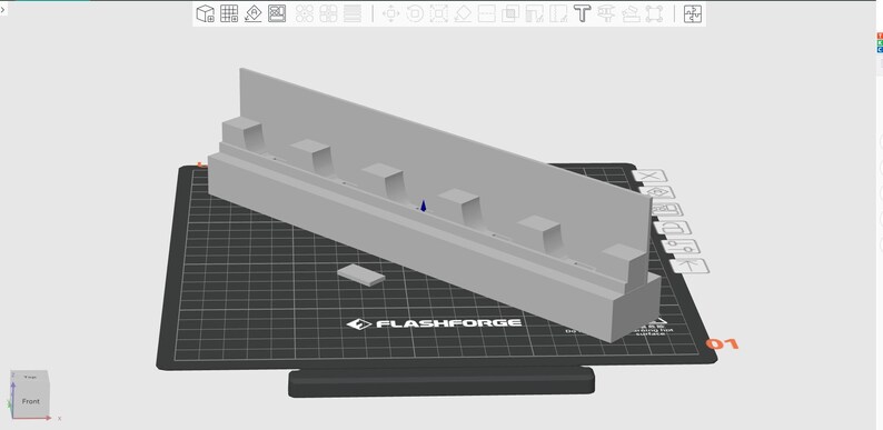 May include: A light gray 3D-printed object, possibly a component or model, featuring a rectangular base with a raised section and several small, square protrusions. It sits on a black grid-patterned surface with the "FLASHFORGE" logo.