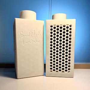 May include: Two off-white rectangular objects with cylindrical tops. One has a honeycomb pattern, the other has the text "Band Made Laser Shop". The objects are on a white surface with a blue background.