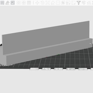 May include: A gray rectangular object with a raised back and a lower base, possibly a shelf or display stand. It sits on a black grid-patterned surface, with a black rectangular piece to the left. The design appears to be a 3D model.