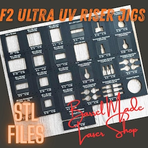 May include: A black rectangular F2 Ultra UV Riser Jig template featuring various cutouts for crystal shapes, including rectangles, hearts, and octagons. The surface is printed with white grid markings, coordinate labels, and text such as Crystal Jig.