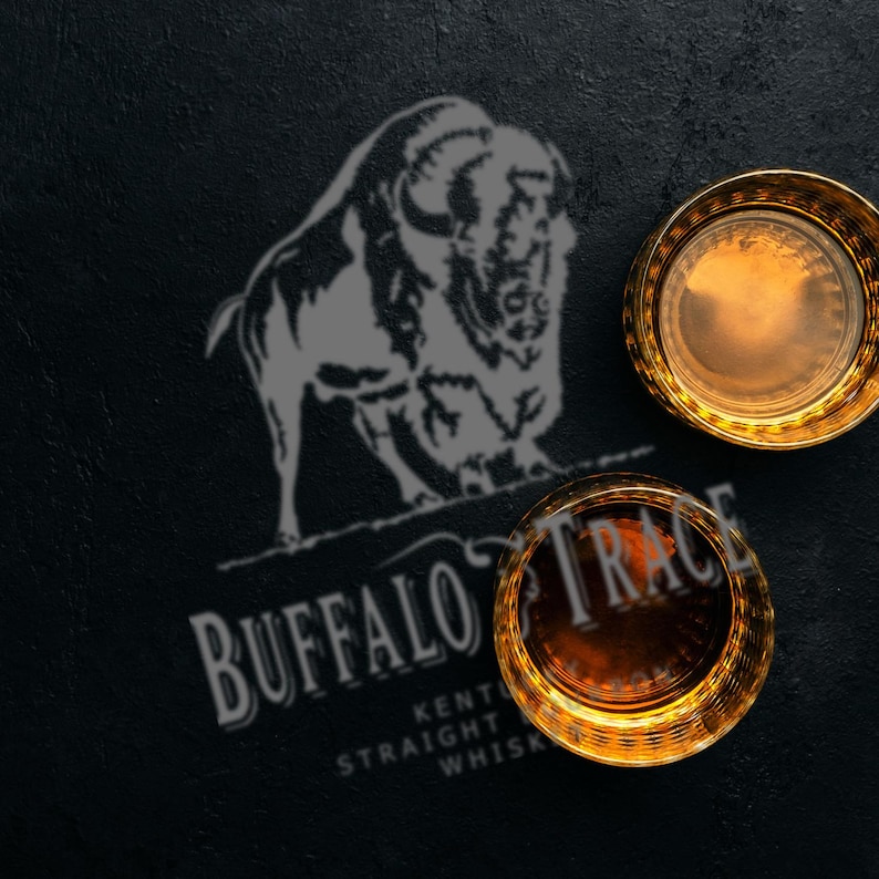 May include: Two gold-rimmed whiskey glasses filled with amber liquid sit on a dark surface. The Buffalo Trace logo and a bison silhouette are visible. The text reads "Kentucky Straight Whiskey."