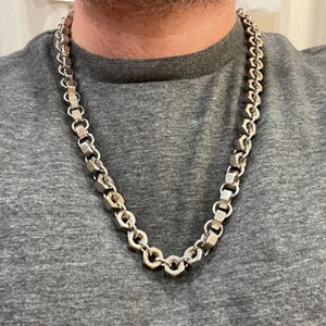 Puede incluir: Un collar de cadena de plata hecho de eslabones hexagonales. La cadena la lleva puesta una persona, pero su rostro no es visible.
