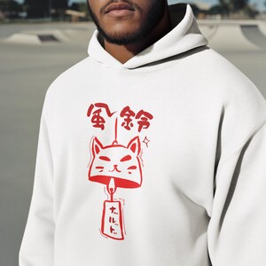 May include: White hoodie with a red graphic of a cat bell and Japanese text. The design includes a cat face, bell, and additional Japanese characters. The hoodie has a drawstring hood and a kangaroo pocket.
