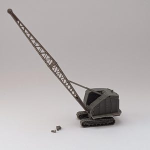 Può includere: Un modello grigio di una gru con un braccio lungo e articolato. La gru è su un set di cingoli e ha una piccola cabina sul retro.