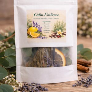 May include: A white pouch with a clear window, labeled "Calm Embrace." The label features illustrations of eucalyptus, lavender, lemon, rosemary, and vanilla. The pouch contains dried herbs, a slice of orange, and cinnamon sticks, suggesting a natural product.
