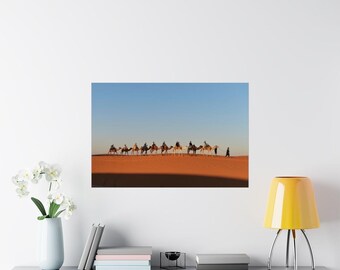 Puede incluir: Una fila de camellos llevando gente a través de un paisaje desértico. Los camellos caminan en fila india, con los jinetes sentados en sus lomos. El desierto es de color arena y el cielo es azul claro.