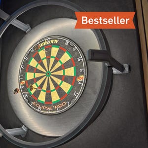 Puede incluir: Un tablero de dardos con un esquema de color negro, verde y rojo, montado en una pared. El tablero de dardos está rodeado por un marco de metal y tiene la palabra "Unicorn" en él. La imagen también incluye la palabra "Bestseller" en una pancarta roja.