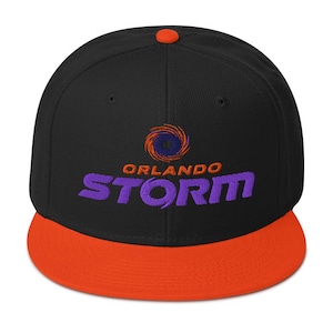 Può includere: Cappellino da baseball nero e arancione a tesa piatta con la scritta "ORLANDO STORM" ricamata in viola. Il cappellino presenta un logo circolare sopra il testo, con la parte superiore nera, la visiera arancione e un piccolo bottone arancione.
