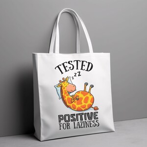 May include: White canvas tote bag featuring a cartoon giraffe sleeping on a pillow. The bag has black text that reads "TESTED ZZZ POSITIVE FOR LAZINESS".