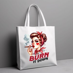 Puede incluir: Bolso tote blanco con una ilustraci&oacute;n retro de una mujer con un pa&ntilde;uelo de lunares rojos y una mejilla en forma de coraz&oacute;n. Est&aacute; fumando un cigarro. El texto "BURN IT DOWN" est&aacute; impreso en rojo y negro.