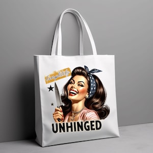 Puede incluir: Bolso tote blanco con una ilustraci&oacute;n retro de una mujer sonriente sosteniendo un cuchillo. El texto "Completely Unhinged" se muestra en el bolso. La mujer tiene cabello oscuro y lleva una diadema.