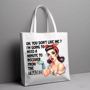 Puede incluir: Bolso tote blanco con una ilustraci&oacute;n retro de una mujer con una diadema roja de lunares y guantes azules. El texto en el bolso dice: "OH, YOU DON'T LIKE ME? I'M GOING TO NEED A MINUTE TO RECOVER FROM THE TRAGED."