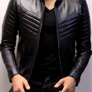 May include: Black leather jacket with a quilted design on the shoulders and upper chest. The jacket has a zip-up front, a stand-up collar, and two zippered pockets. The sleeves are long and fitted. The jacket is worn over a black shirt.
