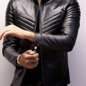 May include: Black leather jacket with a quilted design on the shoulders and chest. The jacket has a zipper closure and a stand-up collar. The sleeves have zippers at the cuffs. The person is holding a lighter.