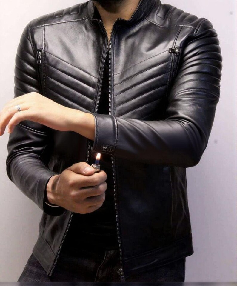 May include: Black leather jacket with a quilted design on the shoulders and chest. The jacket has a zipper closure and a stand-up collar. The sleeves have zippers at the cuffs. The person is holding a lighter.