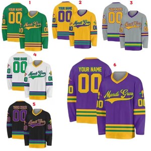 May include: Assorted long-sleeve Mardi Gras jerseys in green, gold, gray, white, black, and purple. Each jersey features a "Your Name" and "00" on the back, with "Mardi Gras" on the front. The jerseys have gold, green, and purple accents.