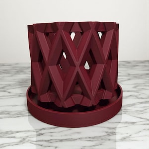May include: A burgundy-colored geometric planter with a matching saucer. The planter features a repeating diamond pattern with open spaces, creating a modern and stylish design. Ideal for indoor or outdoor plants.