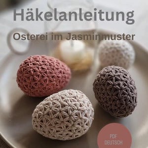 Pode incluir: Um conjunto de ovos de Páscoa de crochê em várias cores, incluindo rosa, bege e castanho, dispostos num prato de tom neutro. Os ovos apresentam um padrão detalhado em forma de estrela. O texto na imagem diz "Häkelanleitung" e "Osterei im Jasminmuster".