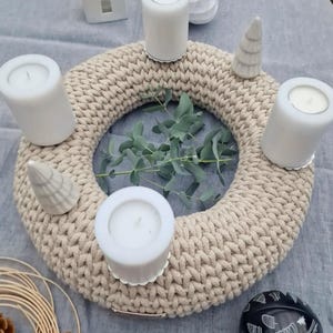 Puede incluir: Una corona de punto grueso beige con cuatro velas blancas y dos peque&ntilde;as figuras de &aacute;rboles de Navidad de cer&aacute;mica. Ramas de eucalipto est&aacute;n en el centro. Una bola decorativa en blanco y negro y otras decoraciones navide&ntilde;as est&aacute;n en el fondo.