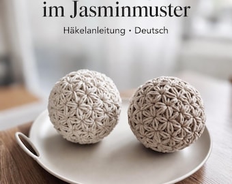 Puede incluir: Dos objetos esféricos de ganchillo con un patrón de punto jazmín en hilo beige claro y beige. El texto superior dice: Dekokugel im Jasminmuster Häkelanleitung • Deutsch. Estos objetos redondos y texturizados están sobre un plato claro.