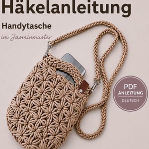 Peut inclure: Une pochette de téléphone crochetée beige avec un motif en point de jasmin, une longue bandoulière tressée avec des clips métalliques et une petite languette en similicuir marron. Le texte indique Häkelanleitung, Handytasche im Jasminmuster et PDF ANLEITUNG DEUTSCH.