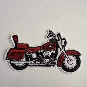 May include: Embroidered patch featuring a red and black motorcycle with saddlebags. The motorcycle has a detailed design with a white border. The patch is likely for jackets, bags, or other apparel.