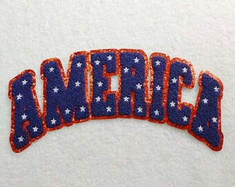 Peut inclure: Un écusson bleu et rouge avec le mot "AMERICA" dans un design audacieux et arqué. Les lettres sont bleues avec des étoiles blanches, soulignées de paillettes rouges. L'écusson est probablement destiné aux vêtements ou aux accessoires.