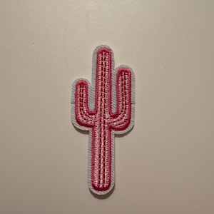 May include: Embroidered cactus patch in bright pink with a white border. The cactus design features detailed stitching, creating a textured appearance. This patch is suitable for adding to clothing, bags, or other fabric items.