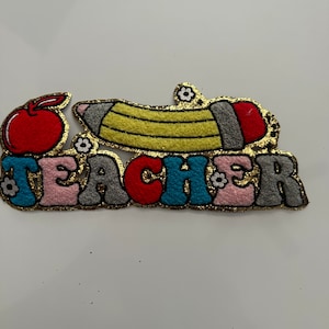 Peut inclure: Un écusson coloré avec le mot "TEACHER" en lettres bulle, représentant une pomme et un crayon. L'écusson a une bordure dorée à paillettes et de petits accents floraux, parfait pour un enseignant.