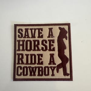 May include: A square patch with the text "SAVE A HORSE RIDE A COWBOY" in dark brown letters. A silhouette of a cowboy is on the right side. The patch has a tan background and a dark brown border.