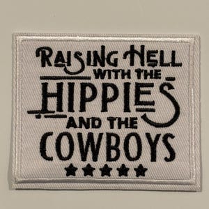 Puede incluir: Parche rectangular blanco con texto bordado en negro que dice: "Raising Hell with the Hippies and the Cowboys". Cinco estrellas negras en la parte inferior. El parche tiene un borde blanco.