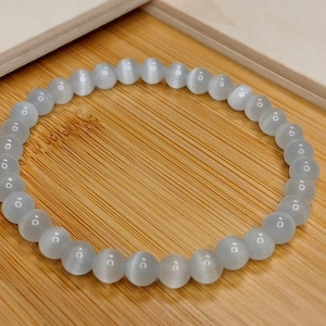 以下が含まれることがあります： 丸いビーズが付いた白い宝石のブレスレット。ブレスレットは、かすかに光る白い石で作られています。