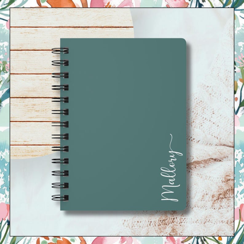 Image of dark greenish blue spiral notebook.  The name Mallory is written vertical along the right edge of notebook.  The last letter has swirl at the end of it.