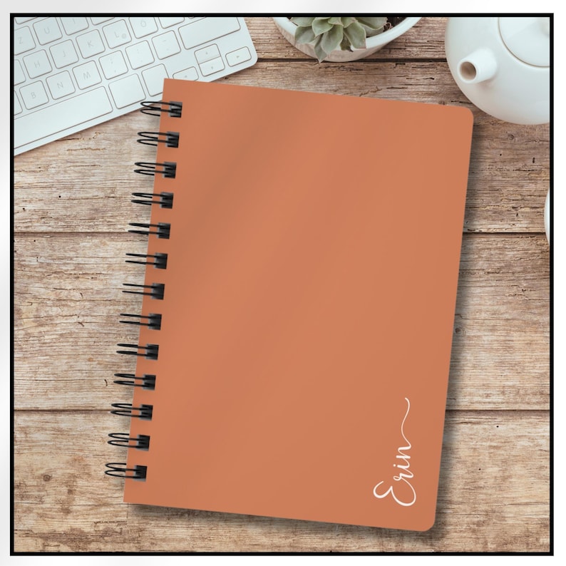Image of an orange spiral notebook.  The name Erin is written vertical along the right edge of notebook.  The last letter has swirl at the end of it.