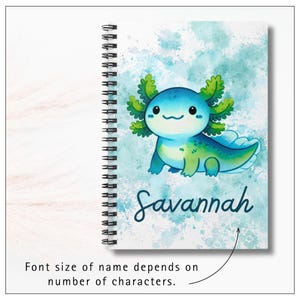 Image of notebook cover.  A cheerful cartoon axolotl with round, smiling face and rosy cheeks. Its body is light teal with darker green spots and shading, and it has large frilly gills on each side of its head in shades of green and teal. Background is a soft watercolor-style wash of teals and green, giving a dreamy, splashy effect. At the bottom, the name “Savannah” is written in playful, dark blue script lettering. Text says, with an arrow, "Font size of name depends of number of characters."