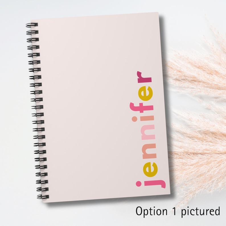 A pink spiral bound notebook with the name 'jennifer' written vertically on the cover in yellow, pink, and red letters.
