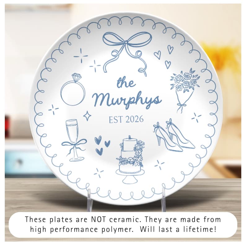 May include: A white polymer plate featuring blue line art illustrations of a bow, a diamond ring, a bouquet, a champagne flute, a three-tiered cake, and high-heeled shoes. The text reads: the Murphys EST 2026. A scalloped border frames the design.