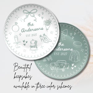 May include: Two round ceramic plates featuring sage green line art illustrations. One plate is white with green designs, the other is green with white designs. Both feature the text "the Andersons EST 2027" surrounded by wedding icons like a ring, cake, and car.