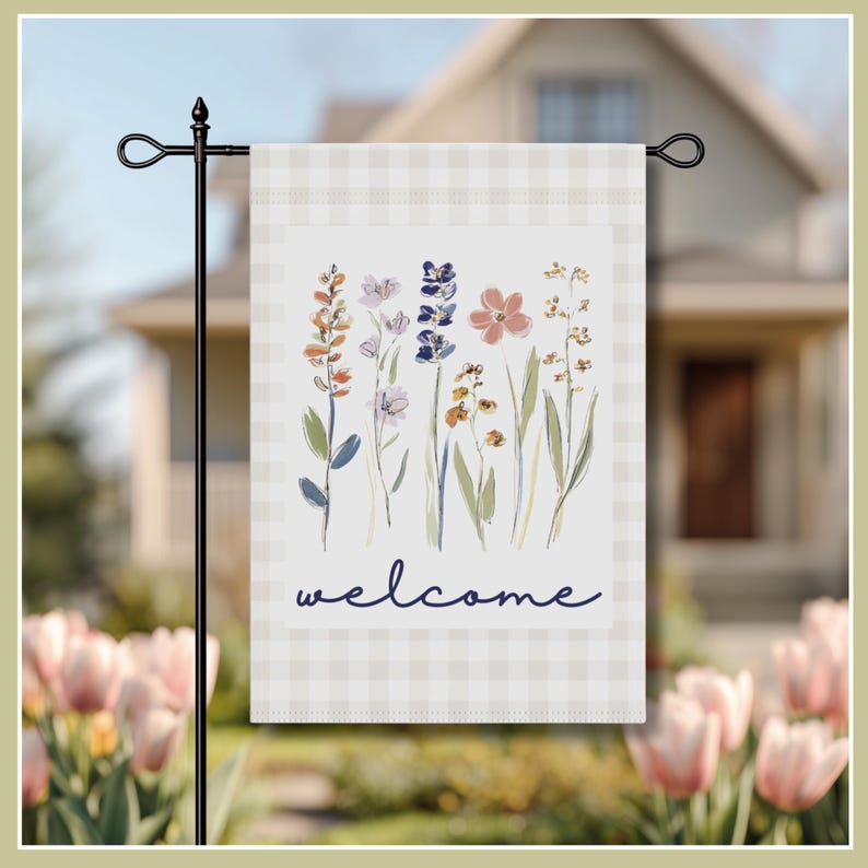 Image of garden flag, featuring a soft watercolor illustration of delicate wildflowers in shades of lavender, peach, and blue. Set against a classic light beige gingham border, the elegant navy script reads "welcome," creating a warm invitation for guests. This durable, double-sided flag is perfect for spring and summer decor, adding a touch of cottagecore aesthetic to your flower beds or walkway.