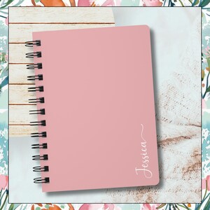 Image of a pink spiral notebook.  The name Jessica is written vertical along the right edge of notebook.  The last letter has swirl at the end of it.