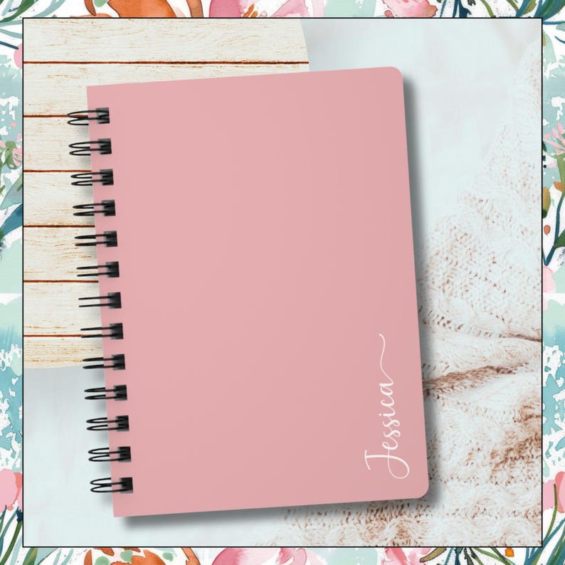 Image of a pink spiral notebook.  The name Jessica is written vertical along the right edge of notebook.  The last letter has swirl at the end of it.
