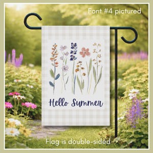 Features our wildflower garden banner in a lush outdoor setting. This image showcases "Font #4" with the cheerful "Hello Summer" greeting in a vibrant navy script. The double-sided print ensures your colorful botanical illustration and welcoming message are visible from both directions. With its soft gingham border and airy watercolor florals, this flag adds an effortless touch of seasonal charm to any garden path or lawn.