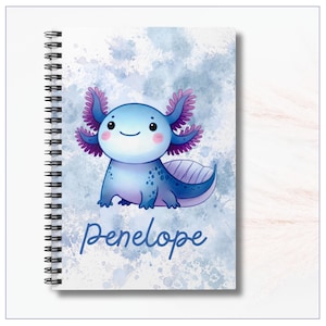 Image of the notebook cover.  A cheerful cartoon axolotl with a round, smiling face and rosy cheeks. Its body is light blue with darker blue spots and shading, and it has large frilly gills on each side of its head in shades of purple and pink. The background is a soft watercolor-style wash of blues and whites, giving a dreamy, splashy effect. At the bottom, the name “Penelope” is written in playful, dark blue script lettering. The notebook is spiral-bound along the left edge.