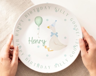 May include: A white ceramic plate featuring a central illustration of a goose wearing a blue patterned party hat and bow tie, accompanied by a light green balloon. The text "Happy Birthday Silly Goose!" and the name "Henry" are printed.