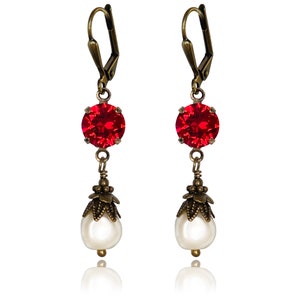 May include: A pair of dangle earrings with a red crystal and a white pearl on each earring. The earrings have a bronze finish.